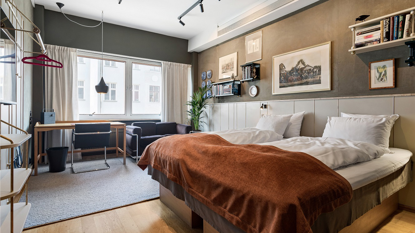 Bild på ett hotellrum, bred dubbelsäng och ljust som sipprar in genom ett stort fönster. 