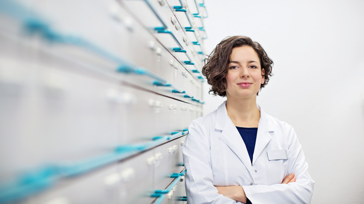 Kvinnlig farmaceut på apotek lutar sig mot hyllor