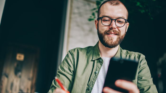 Man tar del av information på sin telefon och antecknar med en orange penna