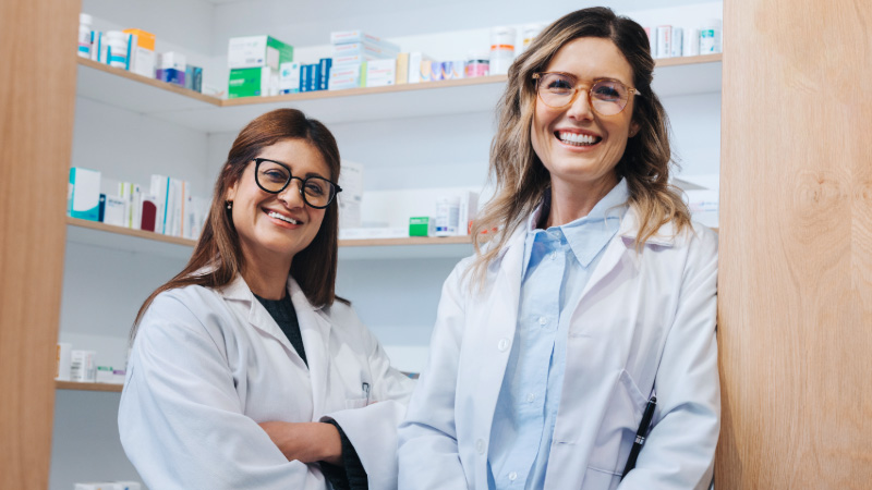 Så fungerar medlemskapet Två farmaceuter i ett läkemedelsförråd iklädda vita rockar. Ser glada ut och tittar in i kameran.