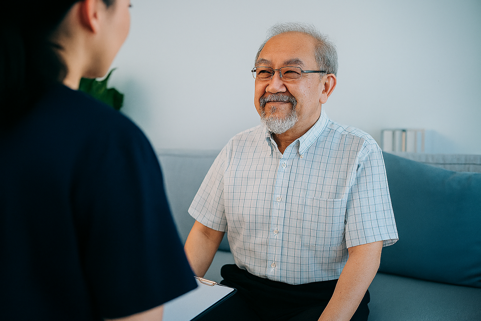 Kommunfarmaceut sitter med ryggen mot kameran och diskuterar något med en äldre patient som ser glad och tacksam ut. 