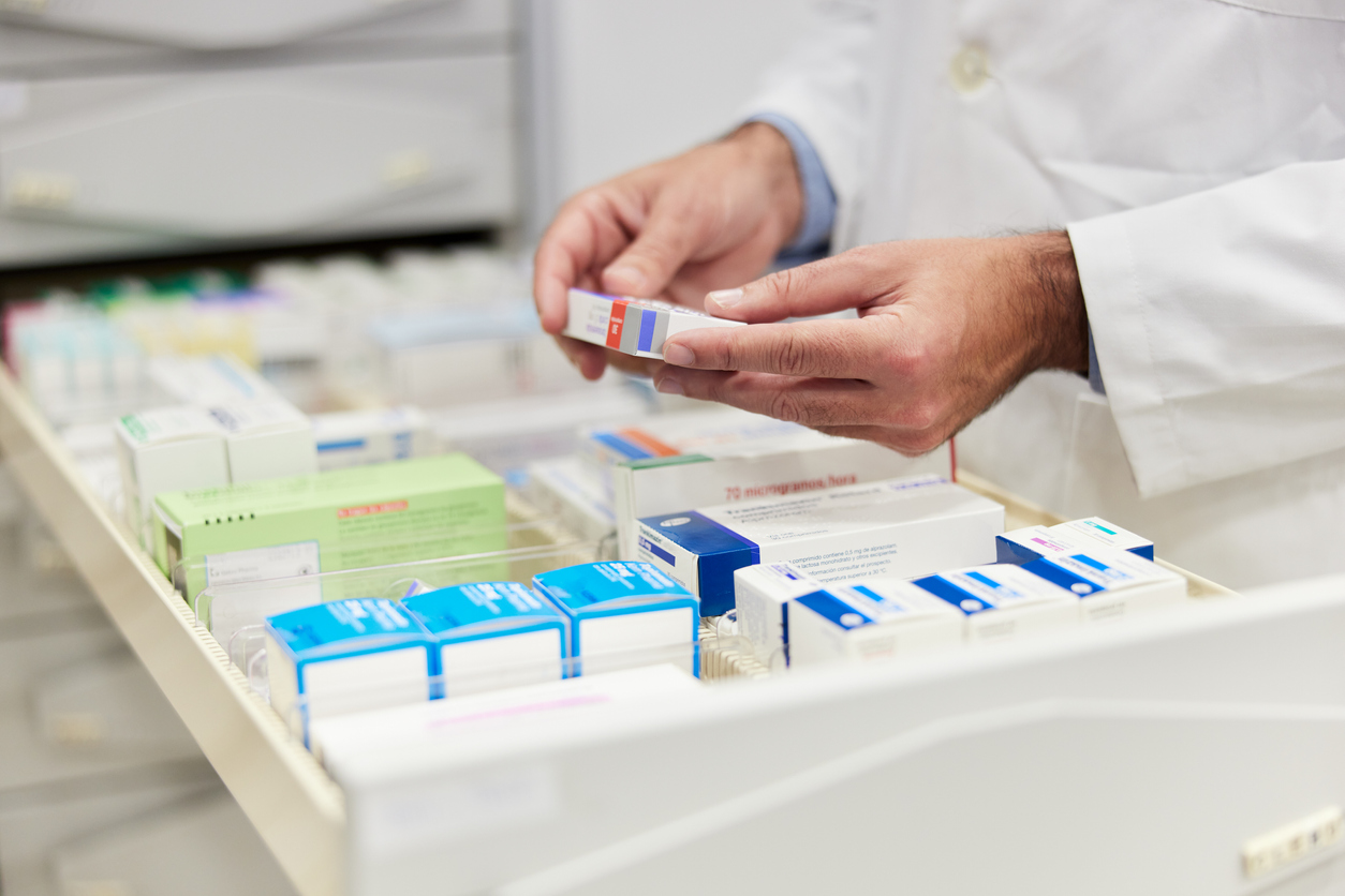 En farmaceut vars händer syns i bild, plockar läkemedel från en låda på apotek