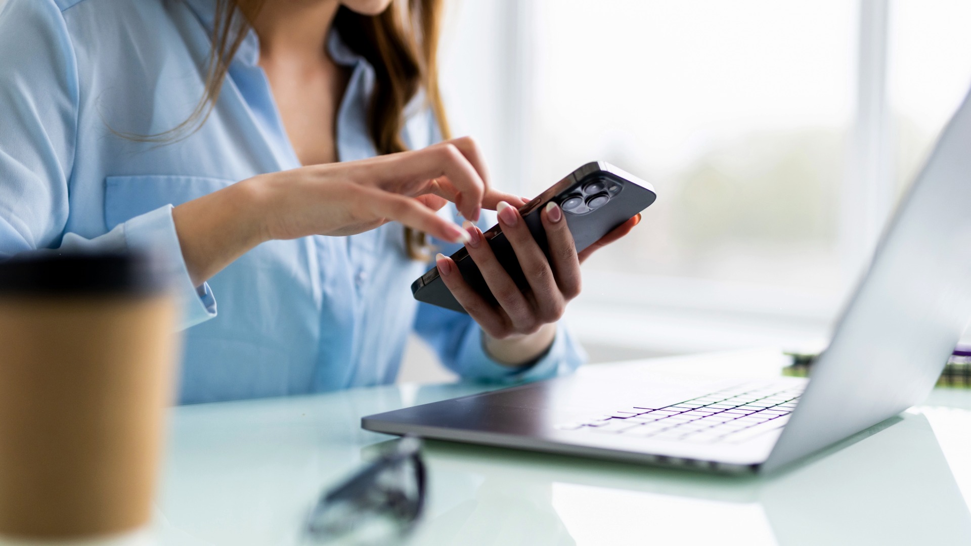 Kvinna framför dator med telefon i handen 