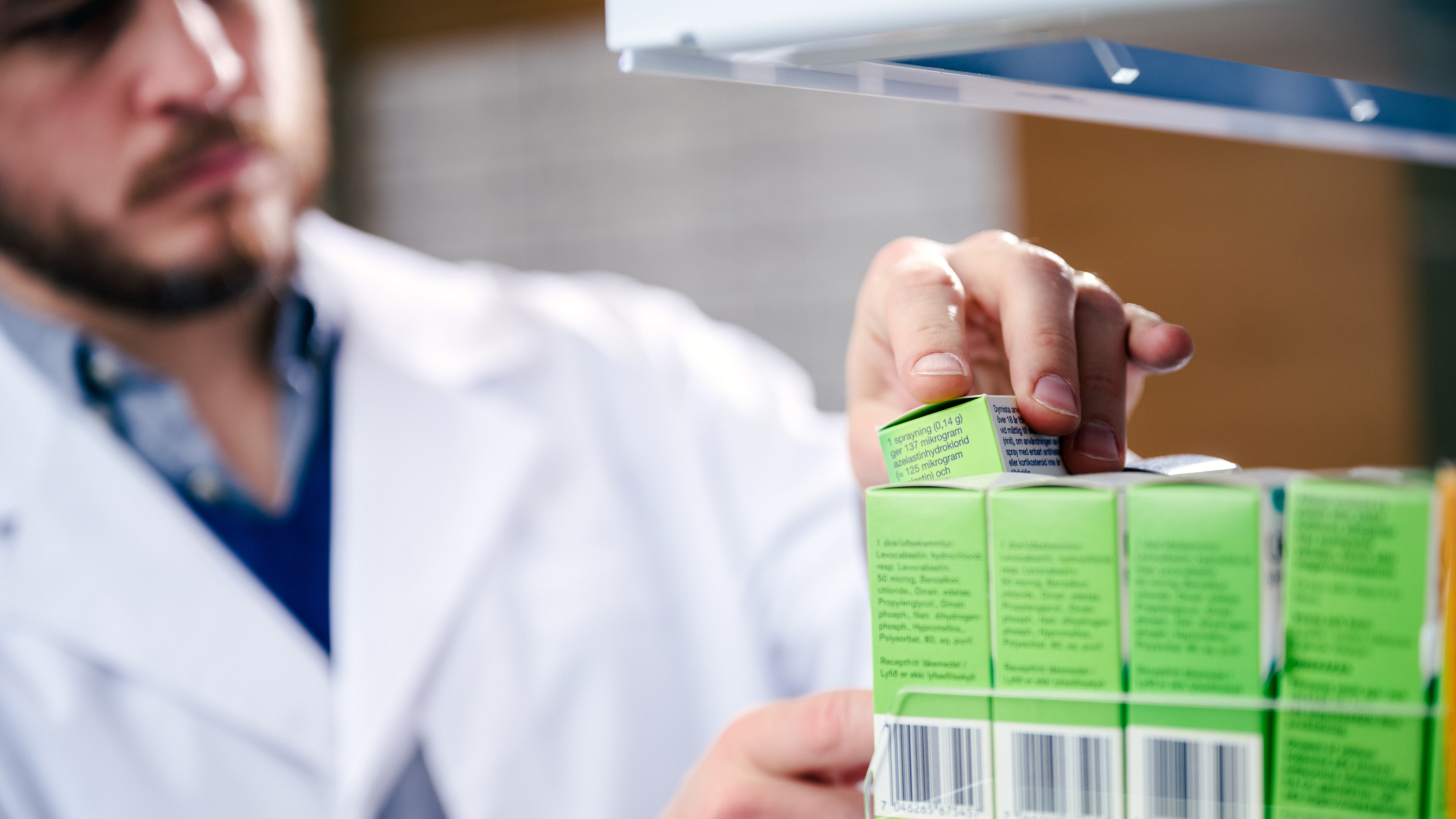 Farmaceut plockar med receptfritt läkemedel på en hylla på ett apotek