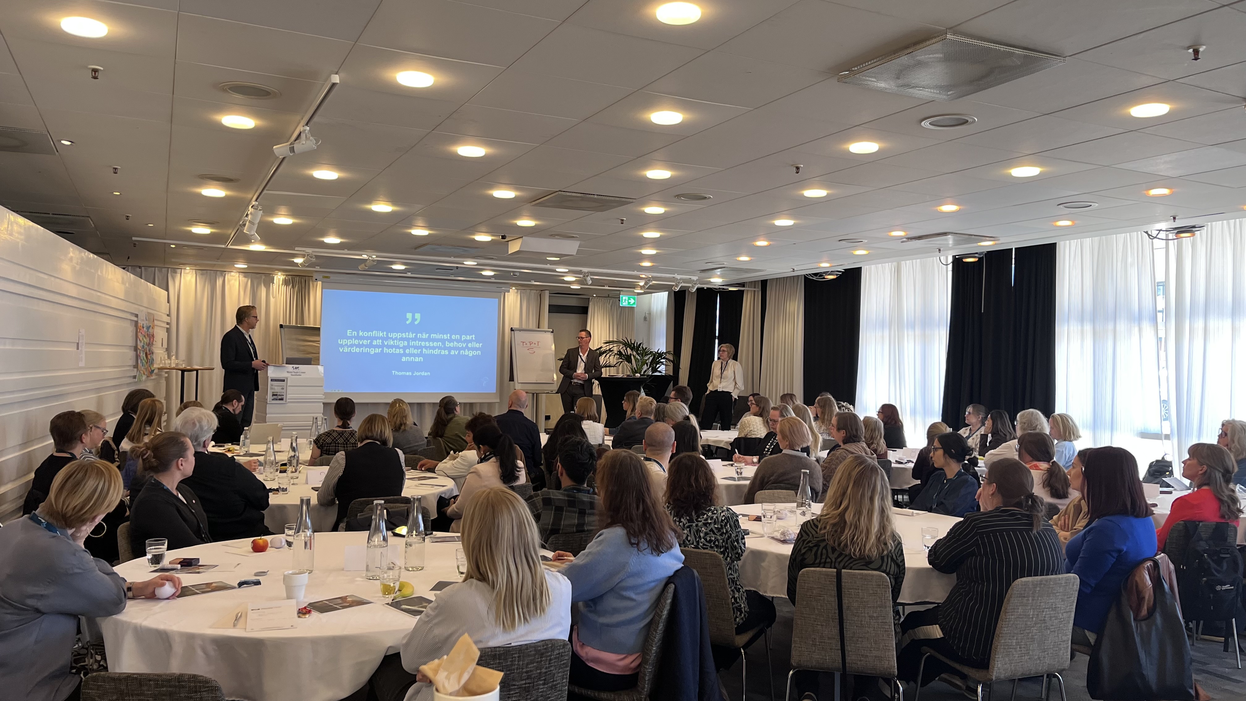 Förtroendevalda på konferens, bild fotad bakifrån man ser de förtroendevalda i rummet och föreläsarna på scenen.